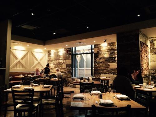 Cozy restaurant interior with wooden tables, chairs, and a mix of diners enjoying their meals in a warm atmosphere.