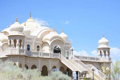 A grand building with ornate architecture, domes, and staircases, set against a clear blue sky.