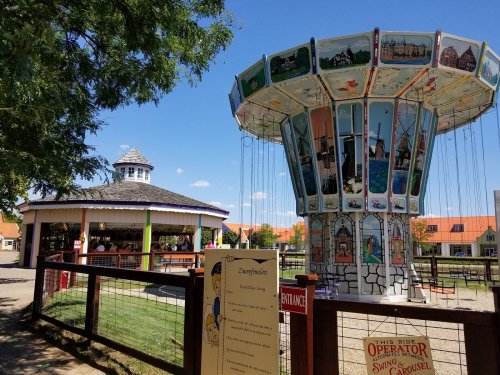 A colorful carousel ride with a gazebo in the background, set in a sunny amusement park.