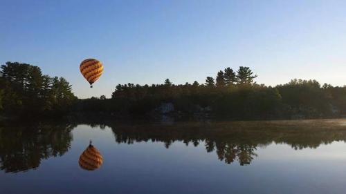 A colorful hot air balloon floats above a calm lake, reflecting the serene landscape and clear blue sky.