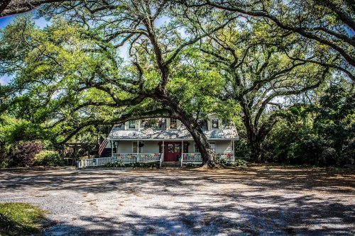 A charming house surrounded by large trees, with a porch and an American flag, set in a peaceful, shaded area.