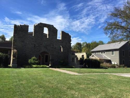 A grassy area featuring a stone ruin and a modern building under a blue sky with scattered clouds.