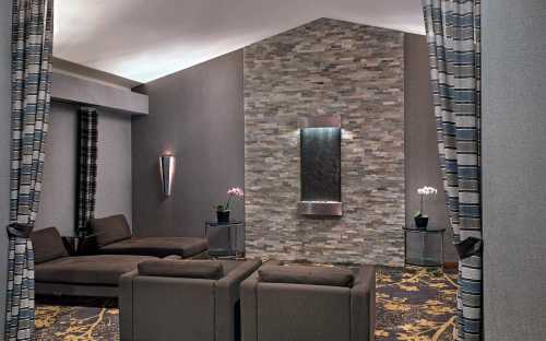 A modern lounge area with a stone wall, water feature, and stylish seating, framed by patterned curtains.