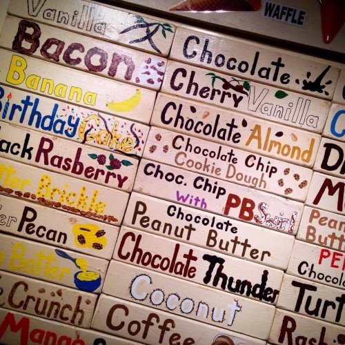 A colorful display of ice cream flavor names painted on wooden boards, including vanilla, chocolate, and more.