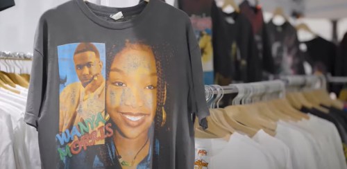 A close-up of a graphic t-shirt featuring two portraits, displayed among other shirts on hangers.