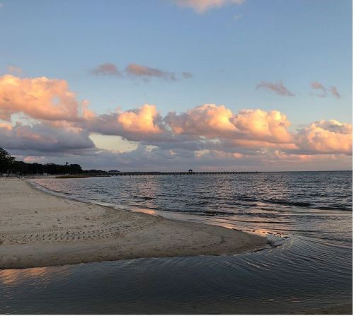 A serene beach scene at sunset, with soft clouds reflecting in the water and gentle waves lapping at the shore.