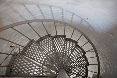 A spiral staircase viewed from above, with a textured metal railing and light reflecting off the white walls.