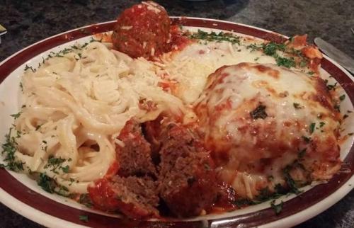 A plate of pasta with creamy fettuccine, meatballs, and cheesy baked lasagna, garnished with parsley.