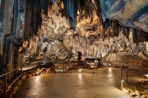 A stunning cave interior with stalactites and stalagmites, illuminated by soft lights, showcasing natural rock formations.