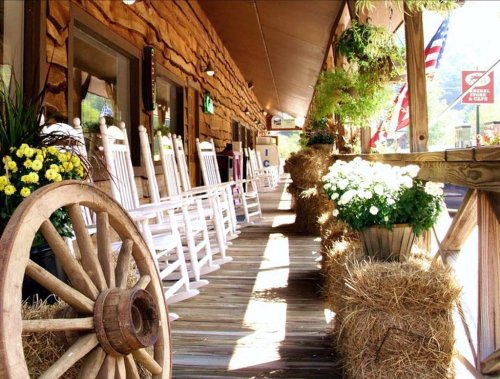 A rustic porch with rocking chairs, potted flowers, and hay bales, creating a cozy, inviting atmosphere.