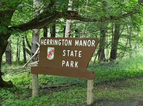 Sign for Herrington Manor State Park surrounded by lush green trees and foliage.