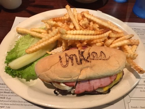 A sandwich with ham, cheese, and vegetables, served with crinkle-cut fries and a pickle on a plate.