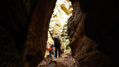 Two hikers explore a narrow canyon, surrounded by towering rock walls and illuminated by natural light.