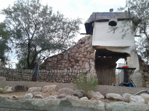 A partially collapsed stone building with a white wall, surrounded by trees and rocky terrain.