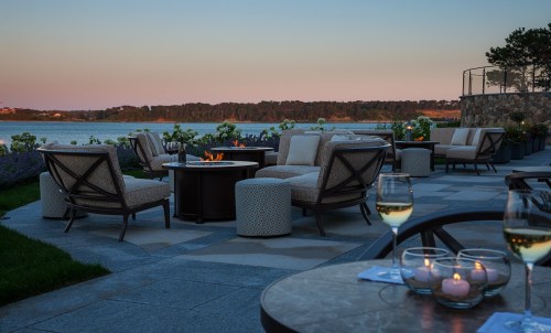 A serene outdoor patio with cozy seating, a fire pit, and a view of the water at sunset.