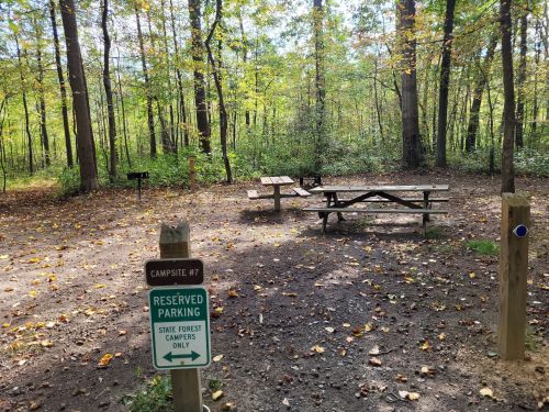 Campsite #7 in a forested area, featuring a picnic table and a reserved parking sign, surrounded by autumn foliage.