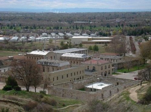 Aerial view of a historic building complex surrounded by trees and residential areas under a cloudy sky.