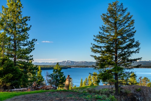 A serene landscape featuring a lake surrounded by trees and distant mountains under a clear blue sky.