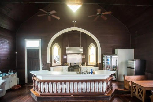 A spacious kitchen with a high ceiling, white island, and dark wooden walls, featuring modern appliances and arched windows.