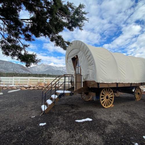 A covered wagon with wooden wheels parked near a scenic landscape of mountains and blue sky.
