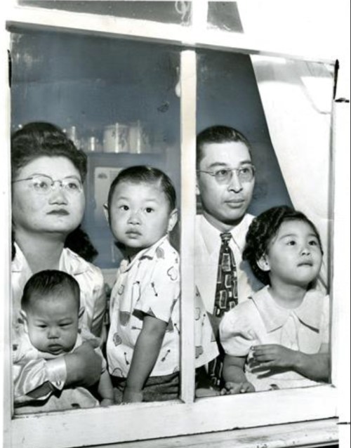 A black-and-white photo of a family looking through a window, including two adults and three children.