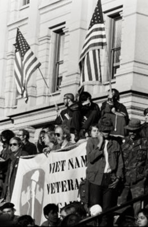 Black and white image of a protest with people holding American flags and a banner for Vietnam veterans.