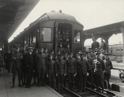 A group of young soldiers in uniform poses in front of a train at a station, with some inside the train.