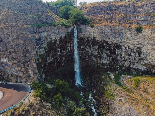 Aerial view of a waterfall cascading down rocky cliffs into a lush green area below.