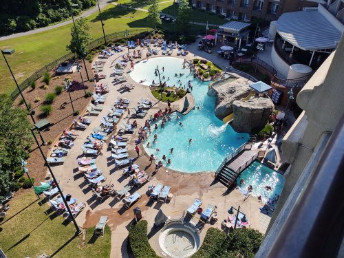 Aerial view of a busy hotel pool area with people swimming, lounging on chairs, and enjoying the sun.