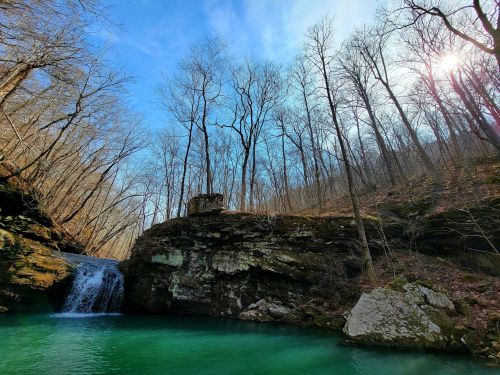 A serene waterfall cascades into a turquoise pool, surrounded by bare trees and a clear blue sky.