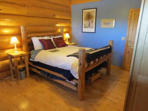 Cozy log cabin bedroom with a wooden bed, blue walls, and warm lighting from bedside lamps.