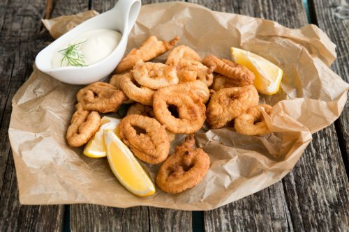 A plate of crispy fried calamari rings with lemon wedges and a small bowl of dipping sauce on parchment paper.