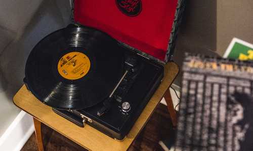 A vintage record player with a black vinyl record on a wooden table, set against a cozy room backdrop.