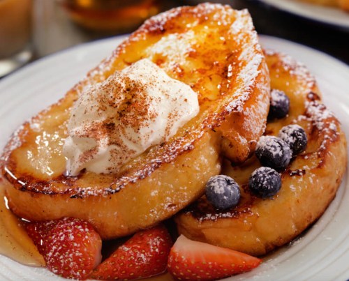 Delicious French toast topped with whipped cream, blueberries, strawberries, and a sprinkle of powdered sugar.