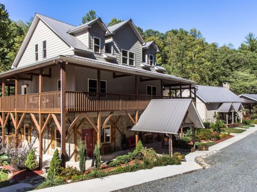 A large, modern house with a balcony, surrounded by trees and landscaped gardens on a sunny day.
