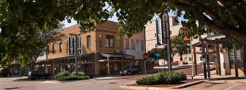 A street view of a small town with shops, banners, and trees, showcasing a welcoming atmosphere.