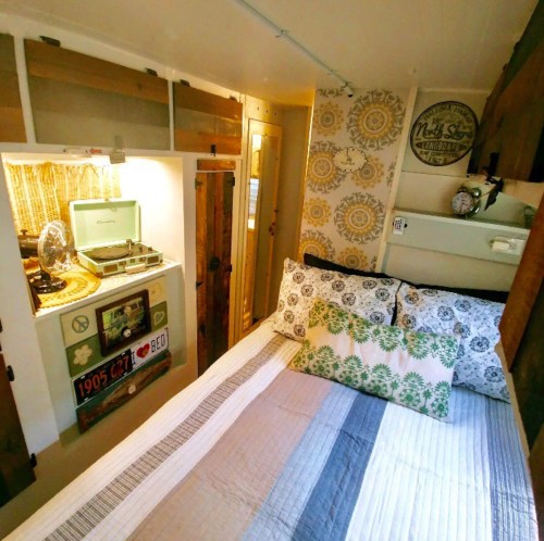 Cozy tiny home interior featuring a bed, patterned walls, and a small kitchen area with vintage decor.