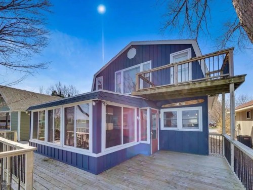 A blue two-story house with a deck, large windows, and a sunny sky in the background.