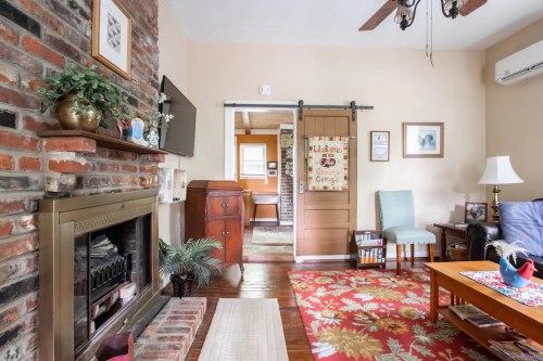 Cozy living room with brick wall, wooden furniture, colorful rug, and a sliding barn door leading to another room.