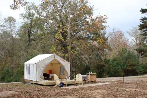 A canvas tent on a wooden platform surrounded by trees, with outdoor seating and a small table nearby.