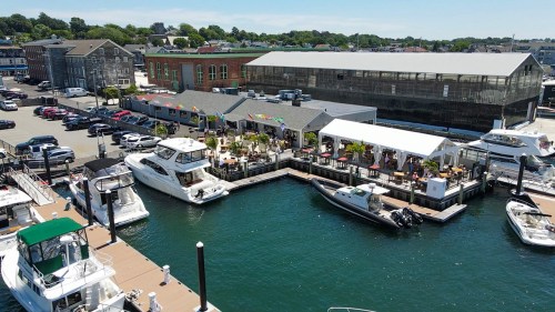 Aerial view of a marina with boats docked, a restaurant with outdoor seating, and buildings in the background.