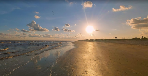 A serene beach at sunset, with golden sand, gentle waves, and a vibrant sky filled with clouds.