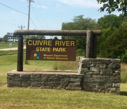 Sign for Cuivre River State Park, featuring a wooden frame and stone base, with nearby road and greenery.