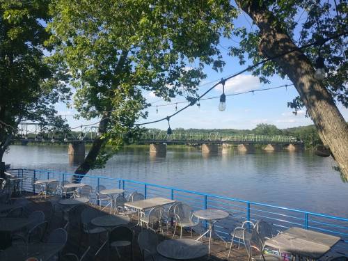 A serene river view with a bridge in the background, surrounded by trees and outdoor seating.