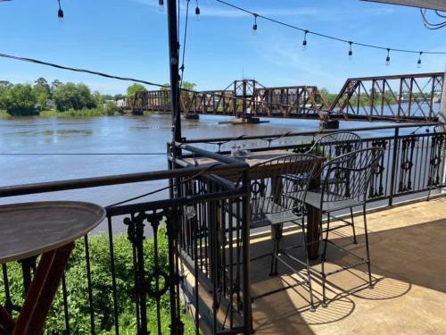A riverside view from a balcony with chairs, overlooking a bridge and lush greenery under a clear blue sky.