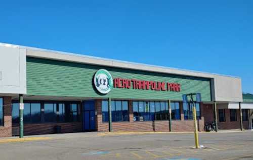 Exterior of a trampoline park building with a green and red sign, clear blue sky in the background.