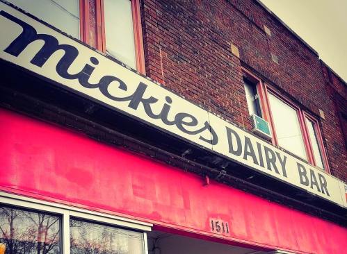 Sign for Mickie's Dairy Bar on a brick building, featuring a bright pink facade and large lettering.