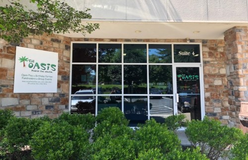 Exterior view of The Oasis office, featuring large windows and a sign, surrounded by greenery. Suite 4 is indicated.
