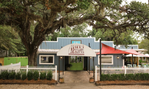 A charming blue pub with a green door, surrounded by trees and a white picket fence, featuring outdoor seating.