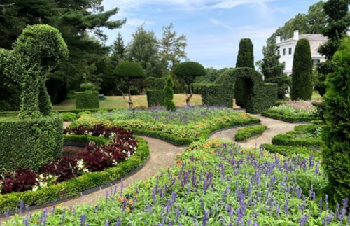 A beautifully landscaped garden with colorful flowers, manicured hedges, and winding pathways under a blue sky.